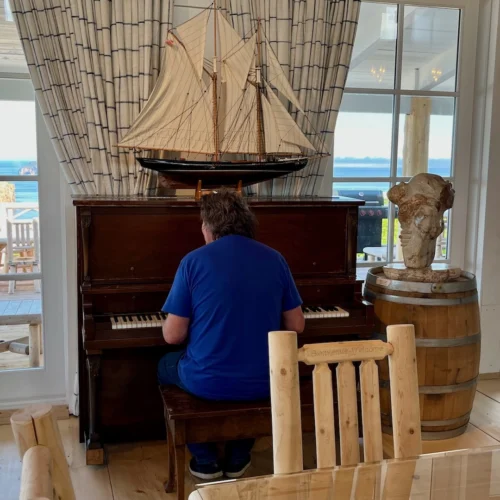 A person seated at the piano in front of a large window overlooking the breathtaking scenery of Percé.